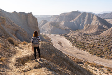 Fototapeta premium A young hiker girl up in the canyon on Rambla de Lanujar in the Tabernas desert, Almería province, Andalusia. Trekking in the desert, lifestyle