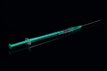 close-up of a syringe on a black shiny surface pulled up with a vaccination serum