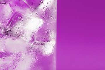 Ice cubes in a glass with refreshing ice water on a pink background.