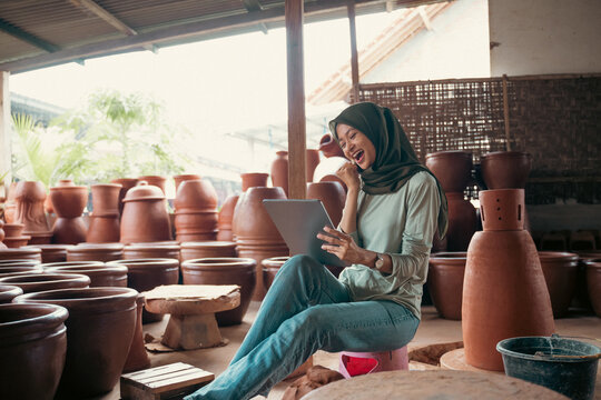 Excited veiled woman uses a tablet in a pottery shop