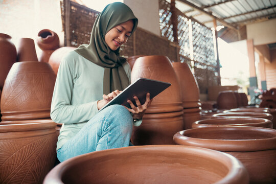 smiling woman in hijab using a tablet between pottery