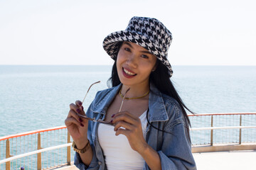 Beautiful asian woman holding black eyeglasses with hat on the sea