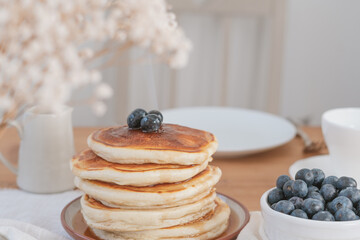 Photo close up stack of pancakes with blueberries and maple syrup. Breakfast table set up. Rustic light and airy feel with white light background and copy space available.