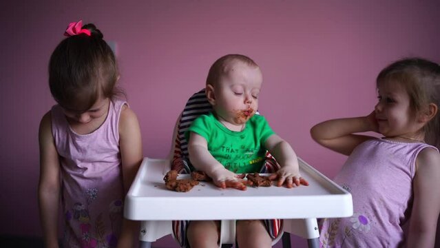 A small child eats chocolate. His face and hands are very dirty. Next to the baby are his sisters. The kid is happy. High quality FullHD footage