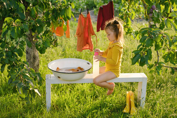 Little girl is doing housework, helping her mother wash clothes in a basin in the garden under a...