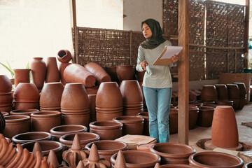 veiled businesswoman counting pottery holding clipboard at ceramic pottery stall