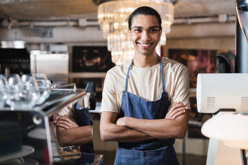 Smiling african american barista crossing arms in cafe.