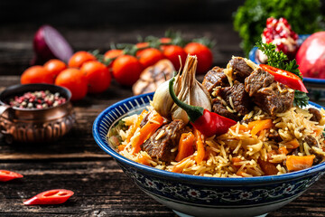 Obraz na płótnie Canvas Traditional uzbek meal called pilaf. Rice with meat on plate with oriental ornament on a dark wooden background, Long banner format. space for text
