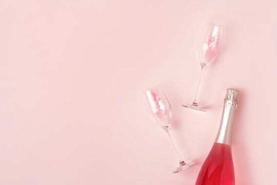 Creative trendy flat lay with pink champagne bottle and flutes filled with pink heart shaped confetti on pastel background. Flat lay, copy space. Happy Valentines Day greeting card.