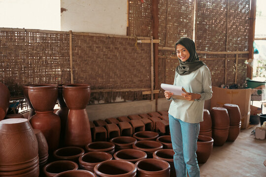 smiling asian muslim businesswoman holding clipboard while at pottery stall