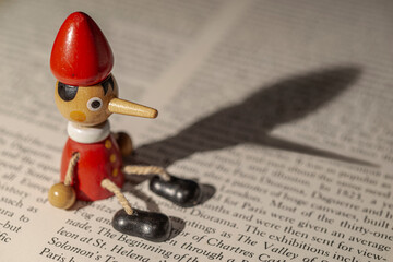 Pinocchio sitting on the text of a book with his shadow cast.