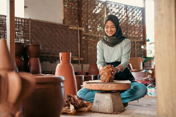 an asian woman in veil makes pottery on a wheel