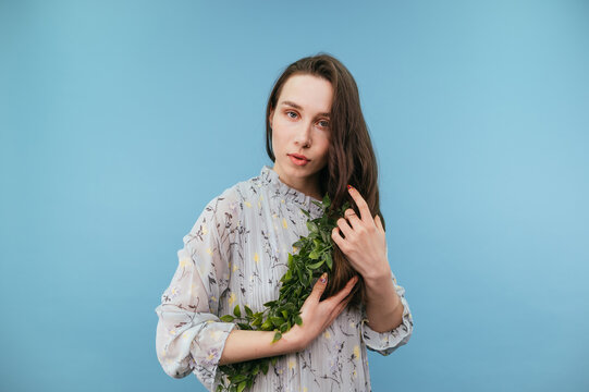 Beautiful brunette woman in a dress with a snug plant in her hands isolated on a blue background, looking at the camera with a serious face.