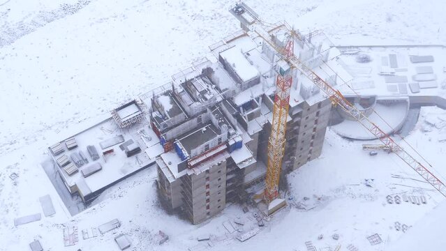 4K.Snow falling and construction site workers build house in dramatic weather conditions in winter.Construction of a panel multi-storey building in the city.Dramatic snowstorm snow fall.