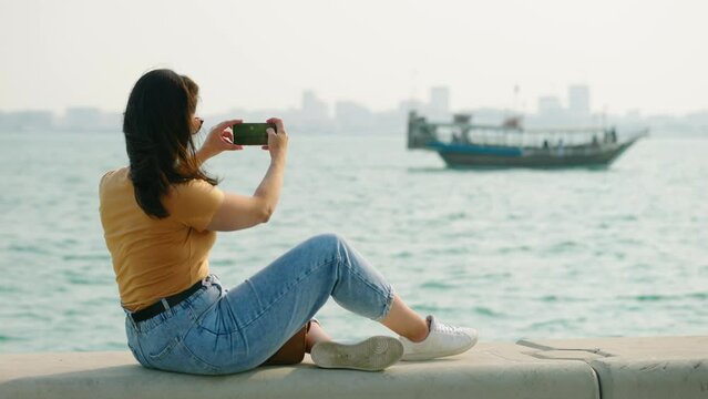 Tourist woman at corniche watching dhow boat passing on west bay at Doha Qatar