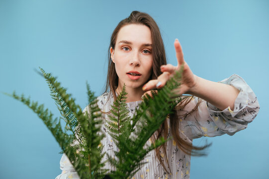 Attractive lady in a dress with dark hair posing at camera with a fern plant, looking at the camera with a serious face, close portrait