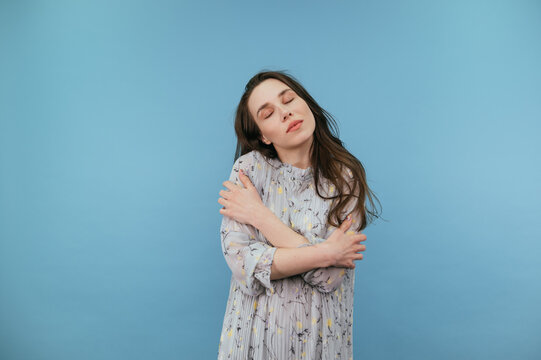 Gentle lady in a frozen dress isolated on a blue background, with closed eyes holding her hands over her shoulders.
