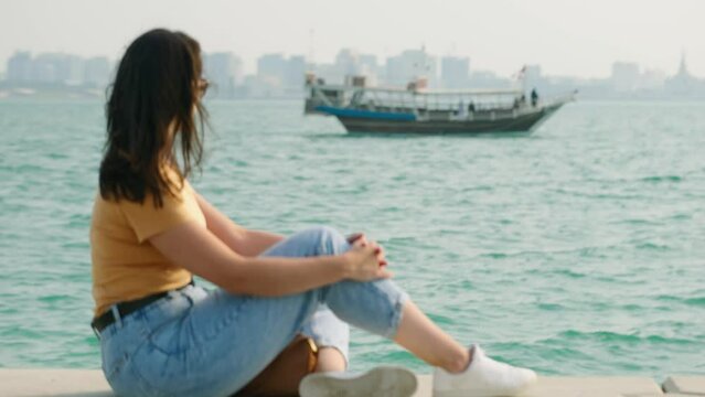 Tourist woman at corniche watching dhow boat passing on west bay at Doha Qatar