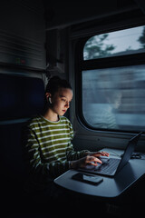 Young business woman in wireless headphones works while traveling by train, sits in a compartment...