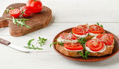 Italian food concept. Open sandwiches with mozzarella, tomatoes and arugula on white wooden background.