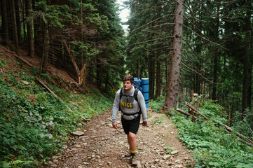 Obraz premium Man hiker in casual clothes with a backpack climbs the mountains with an overnight stay in a large tourist backpack, walks along the trail.
