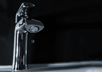 A drop of pure water dripping from the tap. On a dark background.