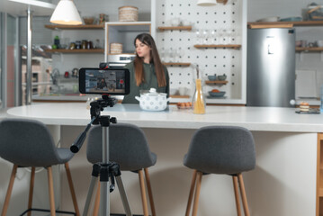 Young vlogger woman vlogging about cooking at her apartment domestic kitchen cook and making video vlog with smartphone as online content creator for internet. Female influencer making a meal.