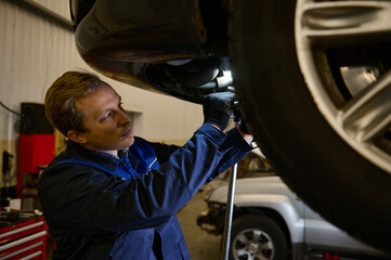 Mechanic checking the alignment of car checking the chassis using a lamp. Car engineer checking tire in maintenance service center. Technician or engineer professional work for customer