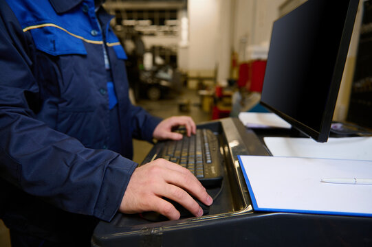 Cropped image of technician, engineer, garage mechanic typing on keyboard, making checklist for repairing cars, conducting diagnostic check of a car during regular warranty maintenance in auto service