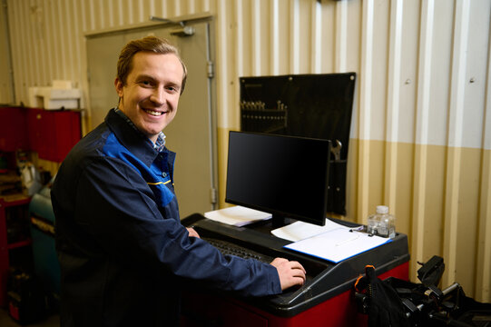 Portrait of a handsome Caucasian man, an auto mechanic, using a PC to diagnose at a car service station. Auto service, car maintenance and repair concept, people and labor concept