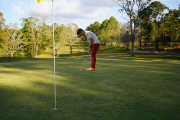 Obraz premium Golf player putting golf ball to hole during sunset or sunrise.