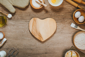 Fototapeta na wymiar Heart shape wooden board near ingridients for prepairing dough