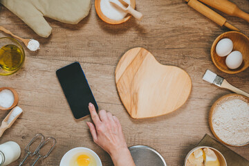 Female hands using smartphone with epmty screen near heart shape wooden board