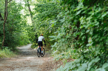 Fototapeta na wymiar Cyclist in sportswear walks on a forest path on a bicycle, rear view.