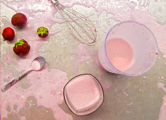 Obraz na płótnie Canvas Making strawberry milkshake smoothie yoghurt pink splatters on a kitchen. High angle flat lay,top view photo