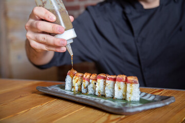 Anonymous man pouring sauce on sushi rolls