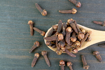 Closeup of Dried Cloves on Wooden Spoon with Some Scattered on Black Table