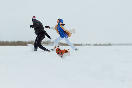 Cheerful couple man and woman running with a dog on a snowy field and having fun. Winter fun with a dog on a walk