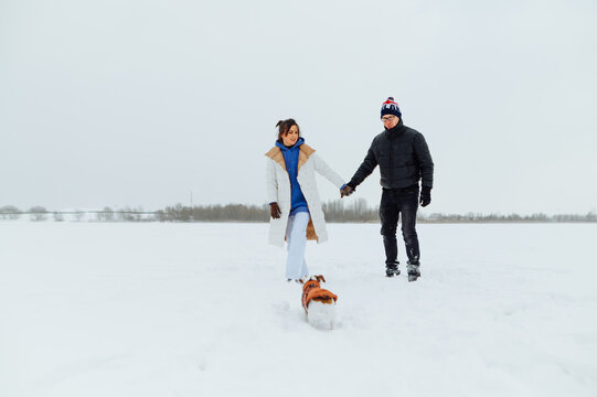 Beautiful couple man and woman holding hands walking on a snowy frozen lake on a walk with a dog breed Jack Russell.