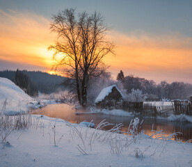 house in the village near the river against the backdrop of the mountains on a winter evening at...