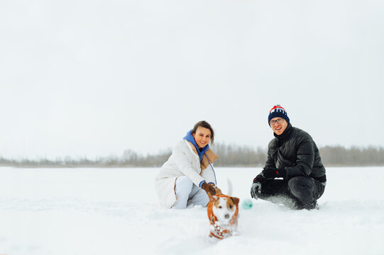 Happy couple playing with dog in winter on snow with smile on face, pet running for ball.
