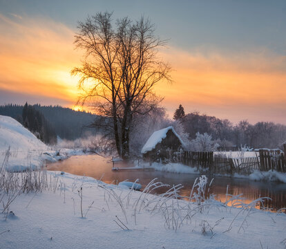 house in the village near the river against the backdrop of the mountains on a winter evening at sunset