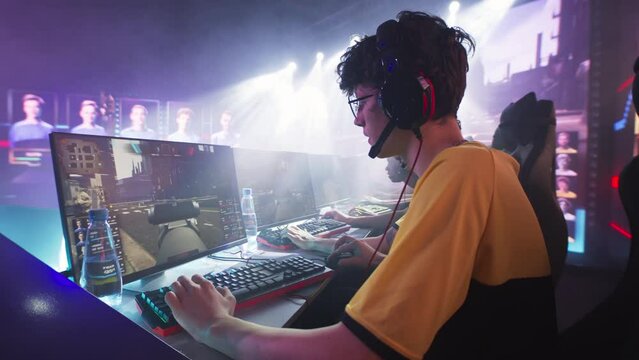 Esportsman gamer in glasses and headphones playing shooter on computer near team while taking park in professional gaming championship battle