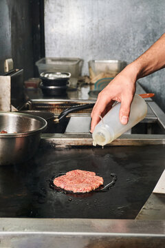 Crop cook pouring oil while frying burger cutlet