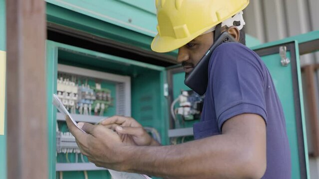 electrical engineer reading or inspecting by talking with colleague on mobile phone in front of circuit board - concept of team work, repair or maintenance service and skilled labour.