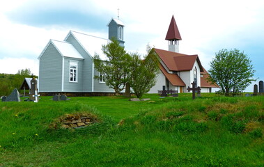 Obraz premium Lutheran church and cemetery in Iceland village. Church in the countryside. Green grass lawn, Icelandic rural scene. 
