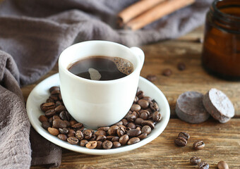 Freshly brewed coffee in a cup on a wooden table. Nearby are a towel, cinnamon, chocolate. Behind is a candle in a jar.