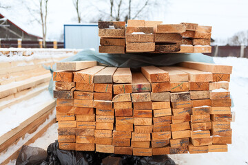 Stacked lumber at construction site. Winter construction of timber house
