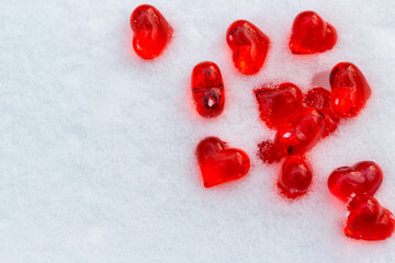 Set of small bright red glass hearts on powdery snow of snowdrift at cold winter day, symbol of romantic love, St. Valentine's Day holiday concept, copy space, top view placer