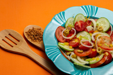 Um prato com salada de vegetais com dois talheres de madeira sobre um fundo alaranjado.